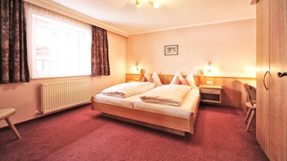 A cozy hotel room with two beds, a desk, and a wardrobe. The room has bright walls and carpeted flooring in warm colors. - Haus Timmelseck - Obergurgl 