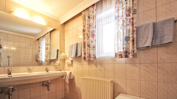 A bright bathroom with tiles and a large mirror. There is a bathtub, a sink, and towels in soft colors. - Haus Timmelseck - Obergurgl 