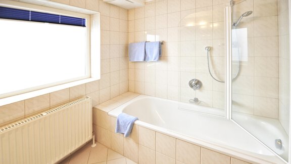 A modern bathroom with a bathtub and a shower. The room is bright and equipped with large tiles. - Haus Timmelseck - Obergurgl 