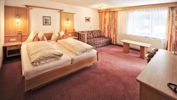 A cozy hotel room with two beds, a couch, and a table. The windows let in a lot of light and the decor is simple and inviting. - Haus Timmelseck - Obergurgl 