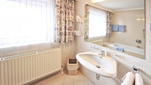 A bright bathroom with a large window and natural light. There is a bathtub, a sink, and white towels. - Haus Timmelseck - Obergurgl 