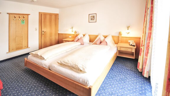A cozy bedroom with two single beds and light wood interior. The room is well-lit and has colorful curtains as well as carpet flooring. - Haus Timmelseck - Obergurgl 