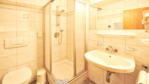 A small bathroom with a shower, a sink, and a toilet. The walls are brightly tiled and there is ample light. - Haus Timmelseck - Obergurgl 