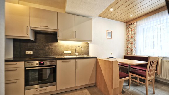 A modern kitchen with light cabinets and a dining table. The room has a window with curtains and good lighting. - Haus Timmelseck - Obergurgl 