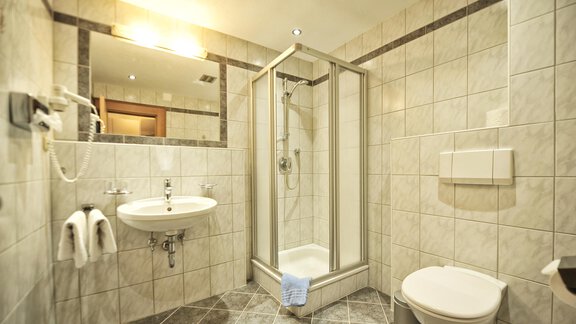 A modern bathroom with tiled walls. There is a shower, a sink, and a toilet, as well as towels. - Haus Timmelseck - Obergurgl 