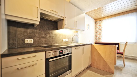A modern kitchen with bright cabinets and a stove. The window lets in plenty of daylight. - Haus Timmelseck - Obergurgl 