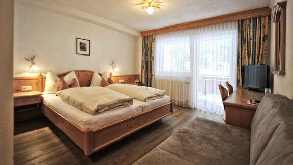 A cozy hotel room with a double bed and a seating area. The large windows provide plenty of daylight. - Haus Timmelseck - Obergurgl 