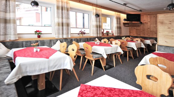 A cozy restaurant with wooden furniture and red tablecloths. The walls are light, and there are large windows that let in a lot of light. - Haus Timmelseck - Obergurgl 