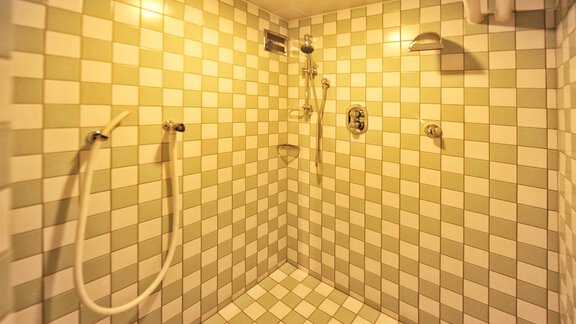 A modern shower with white and green tiles. There are several shower heads and grab bars on the wall. - Haus Timmelseck - Obergurgl 