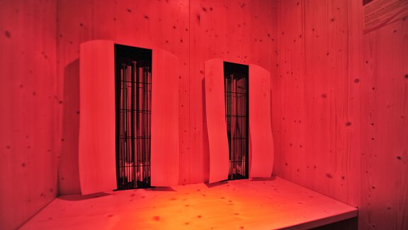 A room with wooden paneling and two infrared lamps. The lighting is in a warm red tone. - Haus Timmelseck - Obergurgl 