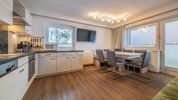 A modern kitchen with a dining area and large windows. The floor is made of wood and the decor is bright and inviting. - Haus Timmelseck - Obergurgl 