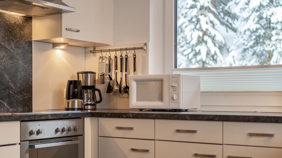 A modern kitchen with bright cabinets and a stone countertop. In the background, there are windows showing snow and trees outside. - Haus Timmelseck - Obergurgl 