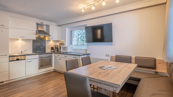 A modern kitchen with a dining table and a cozy seating area. The bright colors and the window create a friendly atmosphere. - Haus Timmelseck - Obergurgl 