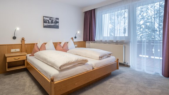 A cozy bedroom with a double bed and two nightstands. The large window front lets in plenty of daylight. - Haus Timmelseck - Obergurgl 