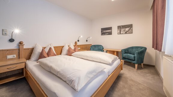 A modern room with a double bed and cozy armchairs. The walls are bright, and there are decorative pictures. - Haus Timmelseck - Obergurgl 