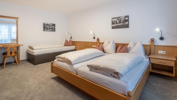 A modern bedroom with two beds and an additional single bed. The decor is simple and cozy, with wooden details and soft lighting. - Haus Timmelseck - Obergurgl 