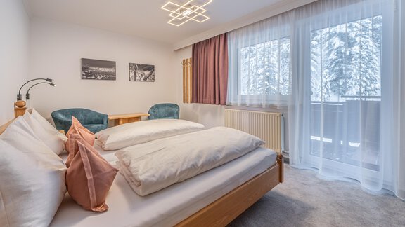 A modern bedroom with a large bed and two cozy chairs. Windows with a view of a snowy landscape. - Haus Timmelseck - Obergurgl 