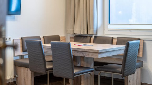 A modern meeting room with a large wooden table and black chairs. The window allows daylight to come in and creates a bright atmosphere. - Haus Timmelseck - Obergurgl 