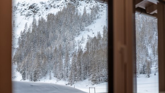 A snow-covered mountain forest with many trees can be seen through the window. The landscape is wintry and quiet. - Haus Timmelseck - Obergurgl 