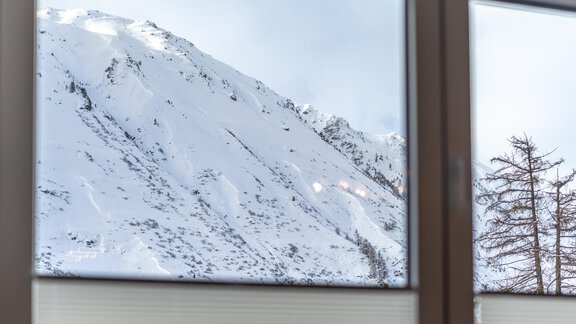 A snow-covered mountain visible through a window. On the right side, a tree without leaves can be seen. - Haus Timmelseck - Obergurgl 
