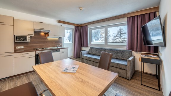 A modern apartment with an open kitchen, a dining table, and a cozy sofa. Large windows provide plenty of daylight and a beautiful view. - Haus Timmelseck - Obergurgl 