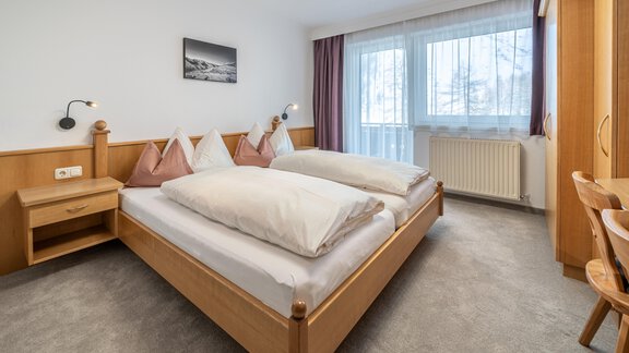 A cozy bedroom with two single beds and a wooden wardrobe. Large windows provide plenty of daylight. - Haus Timmelseck - Obergurgl 