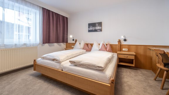 A cozy bedroom with a double bed and light wood interiors. Next to the bed is a table and a chair, as well as a large window with curtains. - Haus Timmelseck - Obergurgl 
