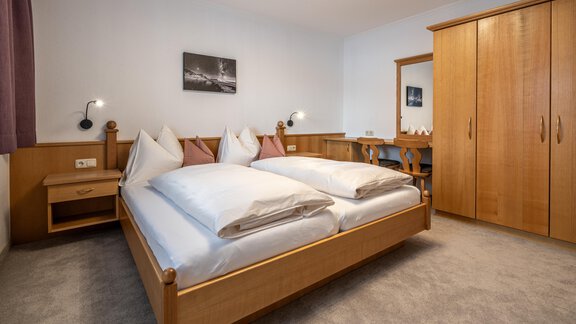 A cozy bedroom with a double bed and wooden furniture. There is a desk and a wardrobe, and the walls are painted in soft colors. - Haus Timmelseck - Obergurgl 