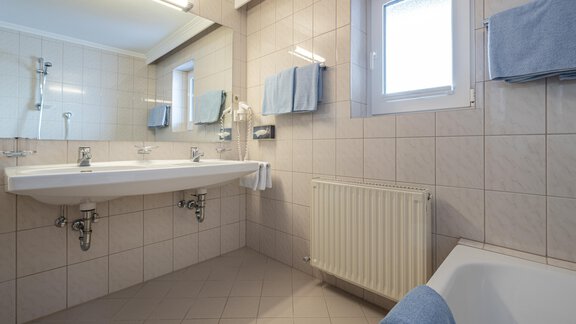 A modern bathroom with a large sink and a window. Clean tiles and towels in soft colors create an inviting atmosphere. - Haus Timmelseck - Obergurgl 
