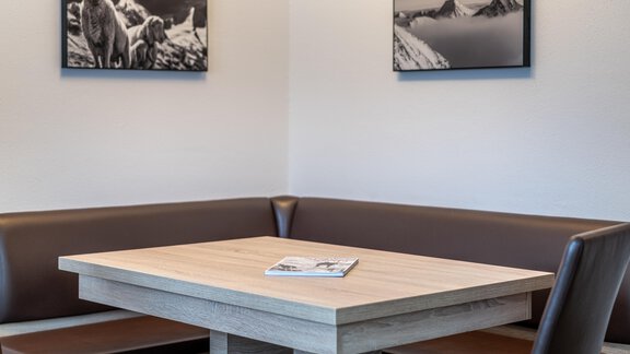 A cozy table with a wooden surface and a bench in a modern room. On the wall hang two black-and-white pictures of mountains and animals. - Haus Timmelseck - Obergurgl 