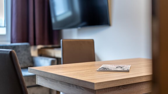 A modern room with a wooden table and two chairs. In the background, there is a television and a window with curtains. - Haus Timmelseck - Obergurgl 