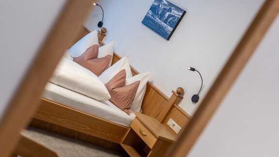 A cozy bedroom with a wooden bed and pink pillows. A picture of a landscape hangs on the wall. - Haus Timmelseck - Obergurgl 