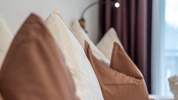 A cozy sofa with cushions in soft colors. In the background, curtains and a light source are visible. - Haus Timmelseck - Obergurgl 