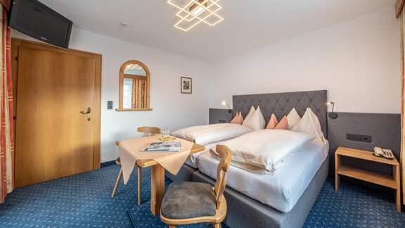 A cozy hotel room with two beds, a table and chairs. A television hangs on the wall, and the lighting is modernly designed. - Haus Timmelseck - Obergurgl 