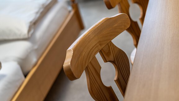 A wooden chair stands next to a bed in a cozy bedroom. The table is also made of wood and conveys a warm atmosphere. - Haus Timmelseck - Obergurgl 