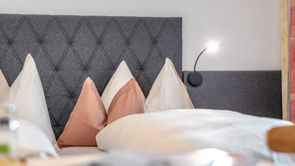 A modern bedroom with a upholstered headboard and decorative pillows. The soft lighting creates an inviting atmosphere. - Haus Timmelseck - Obergurgl 