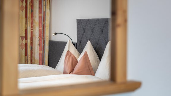 A cozy bedroom with a gray headboard and decorative pillows. The walls are in warm colors and a window frame is visible. - Haus Timmelseck - Obergurgl 