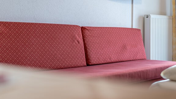 A red sofa with a simple pattern in the living room. In the background, a radiator and a television can be seen. - Haus Timmelseck - Obergurgl 