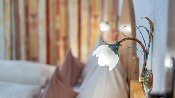 A cozy bedroom corner with a decorative bedside lamp and bright pillows. In the background, colorful curtains can be seen. - Haus Timmelseck - Obergurgl 