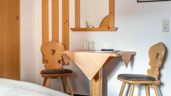 A small table with two wooden chairs in a cozy room. On the wall hang some decorative elements, and there is a mirror above the table. - Haus Timmelseck - Obergurgl 