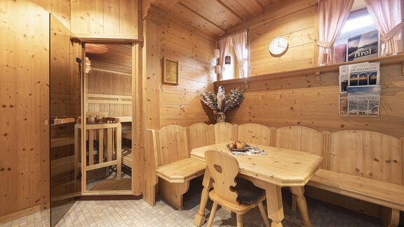 A cozy wooden room with a large dining corner and access to a sauna. The walls and furniture are made of light wood, and the windows are adorned with pretty curtains. - Haus Verwall Appartements - Obergurgl 