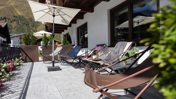 A bright terrace with sun loungers and sun umbrellas. In the background, there are plants and a beautiful view of the mountains. - Haus Verwall Appartements - Obergurgl 