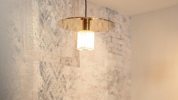 A stylish ceiling lamp hangs on a bright wall. The lighting has a modern design with golden and clear elements. - Haus Verwall Appartements - Obergurgl 