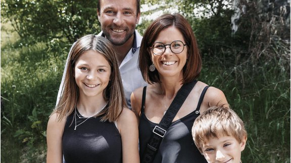 A family is standing outdoors, smiling. In the background, there are trees and a lot of greenery. - Haus Verwall Appartements - Obergurgl 