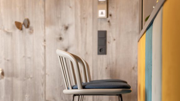 A modern chair stands in front of a wooden wall. The wall is kept neutral and has colorful accents. - Haus Verwall Appartements - Obergurgl 
