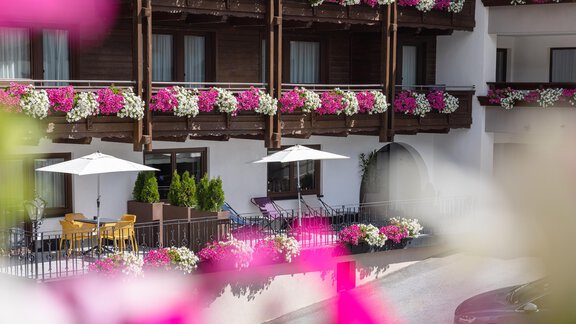 A beautiful hotel view with colorful flower balconies. Tables and sun umbrellas invite you to relax. - Haus Verwall Appartements - Obergurgl 
