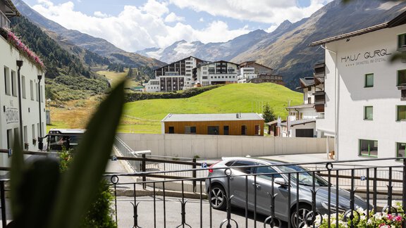 A quiet mountain landscape with modern buildings in the background. In the foreground, there is a gray car and there is a lot of greenery. - Haus Verwall Appartements - Obergurgl 