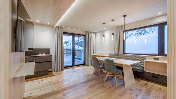 A modern living room with a large window and a dining area. The room features bright wood floors and minimalist furniture. - Hotel-Garni Pirchhütt - Obergurgl 