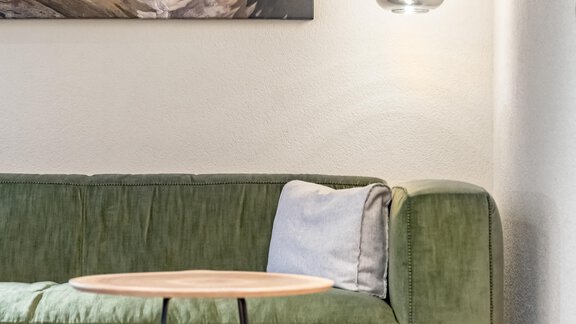 A modern living room with a green sofa and a round table. Above the sofa hangs an elegant lamp and a landscape painting adorns the wall. - Hotel-Garni Pirchhütt - Obergurgl 