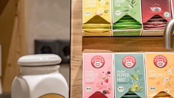 A tea station with various types of tea in colorful packaging, as well as a ceramic teapot. The area is designed to be modern and inviting. - Hotel-Garni Pirchhütt - Obergurgl 